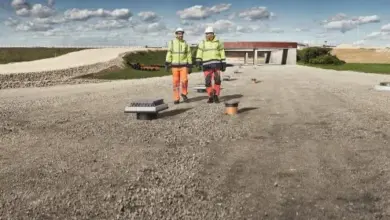 Dva dělníci na štěrkové ploše u drenážních materiálů venku.