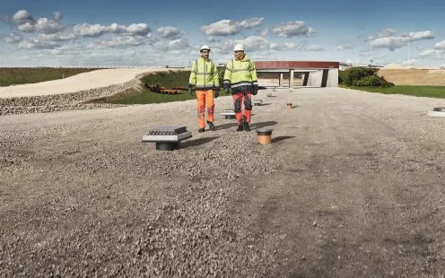 Dva dělníci na štěrkové ploše u drenážních materiálů venku.