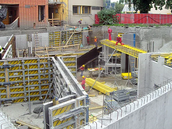 Staveniště s pracujícími dělníky a betonovými tvary.