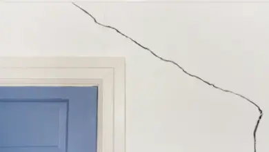 Velká prasklina v bílé sádrokartonové stěně vedle modré dveří.