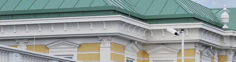 Detail bílé střešní římsy pod zelenou střechou na žluté fasádě.