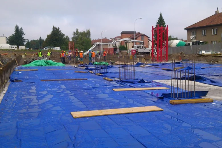 Staveniště s čerstvým betonem chráněným před deštěm plachtami.