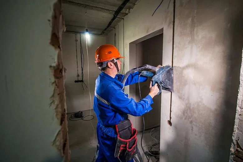 Stavebník řezá drážku ve zdi pro kabeláž pomocí elektrického nástroje.