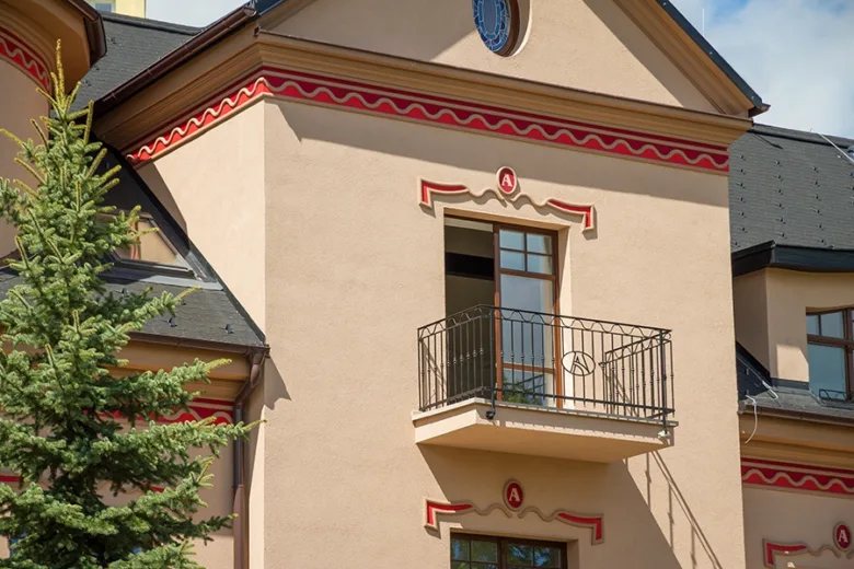 Střešní římsa na fasádě budovy s červenobílým ornamentem.