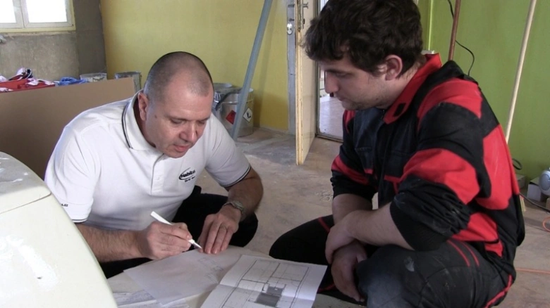 Dva muži studují plány pro instalaci sádrokartonové příčky.
