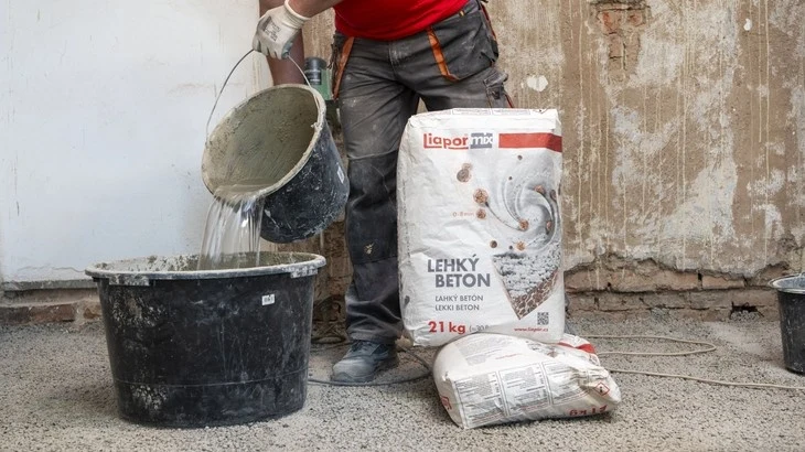 Pracovník míchá betonový roztok vedle sáčků lehkého betonu.
