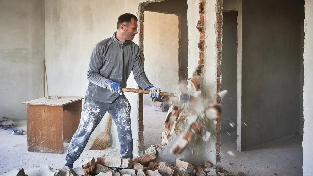 Muž rozebírá nosnou cihlovou stěnu v budově.
