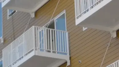 Balkón s bílým zábradím na žluté fasádě bez stropu.