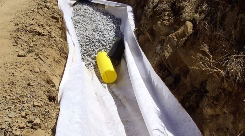 Geotextil v příkopu s kamenivem pro drenážní systém.