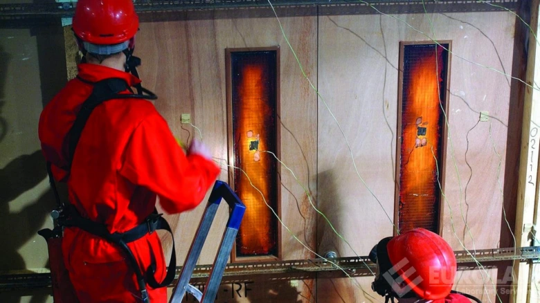 Zkušební hořlavost dřevěného materiálu s pracovníky v ochranném obleku.