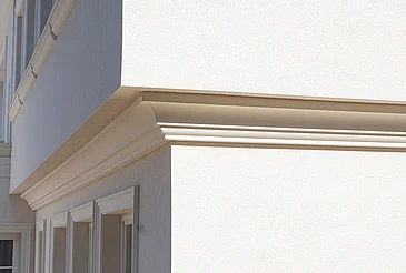 Detail bílé střešní římsy na rohu budovy.