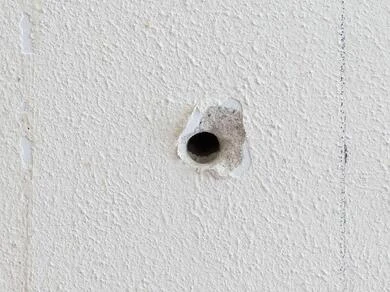 Malé poškození omítky s odhaleným betonem na zdi.