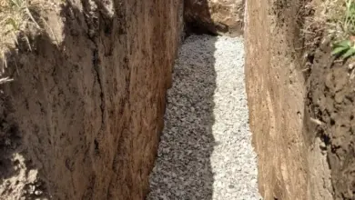 Přímočarý příkop s kamenivem pro drenáž kolem domu.