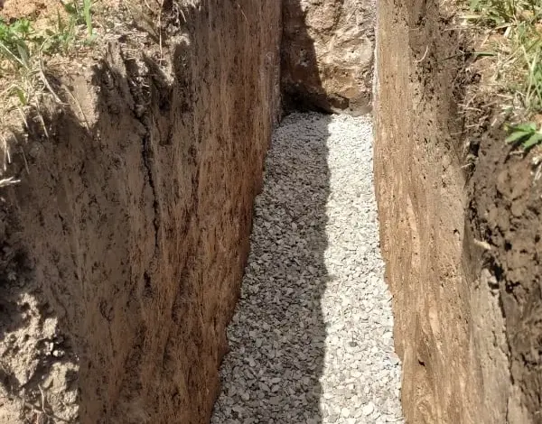 Výkop pro odvodnění základů domu s vrstvou štěrku.