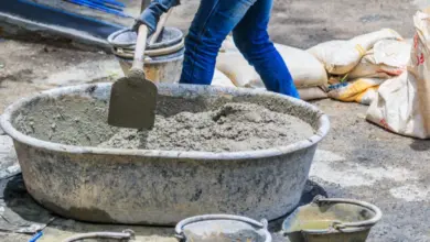 Pracovník míchá beton v kbelíku s lopatkou na staveništi.