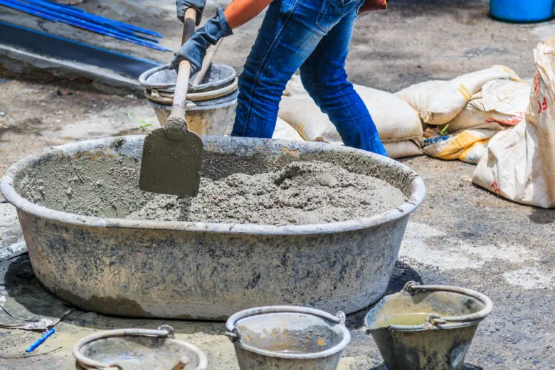 Pracovník míchá beton v kbelíku s lopatkou na staveništi.