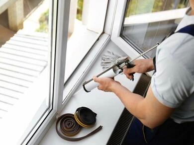 Muž utěsnuje parapet okna pěnovou pistolí proti průvanu.