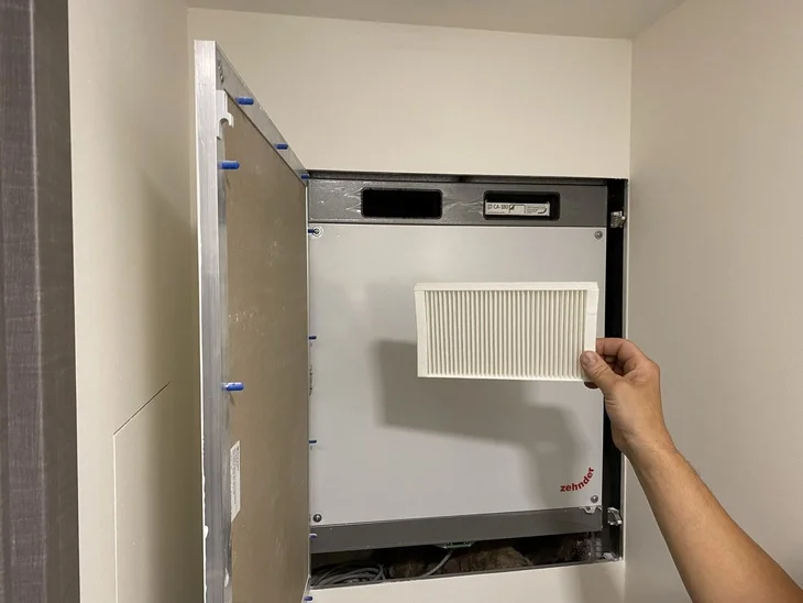 Ruční výměna filtru v větrací šachtě uvnitř panelového domu.