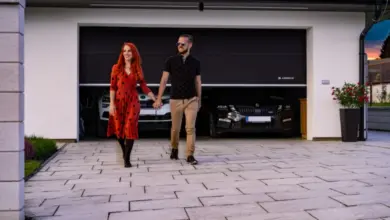Muž a žena jdou před garáží s dvěma auty uvnitř.