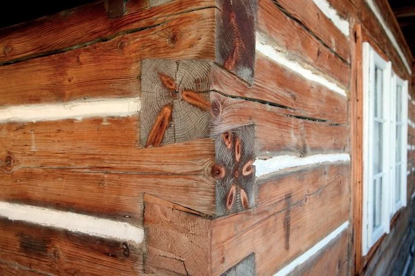 Detail spojení trámů v rohu dřevěného domu s viditelnou štukováním.