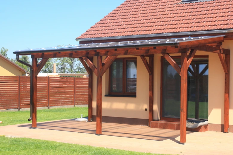 Dřevěná pergola přistavěná k domu v zahradním prostředí.