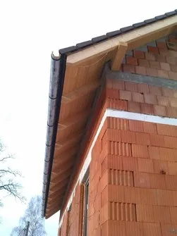 Detail střešní římsy s odvodňováním na dřevěném domě.