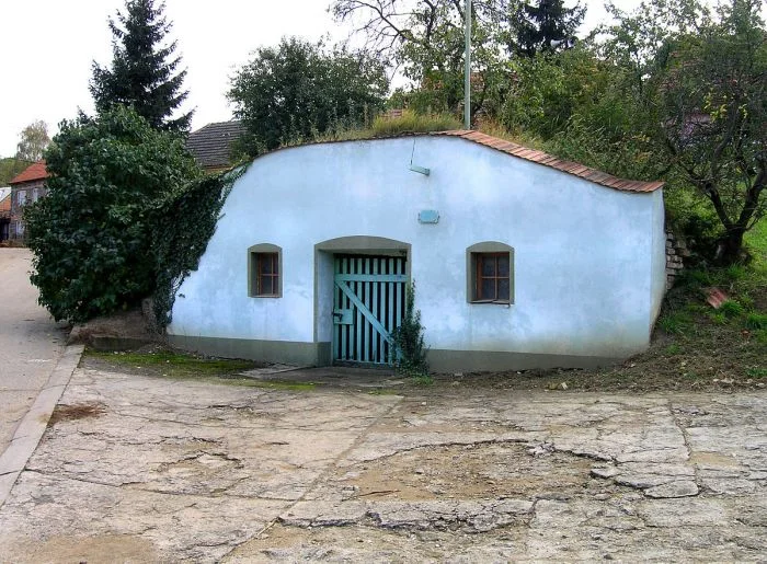 Bílý vinný sklep s zelenou dveřmi a okny.