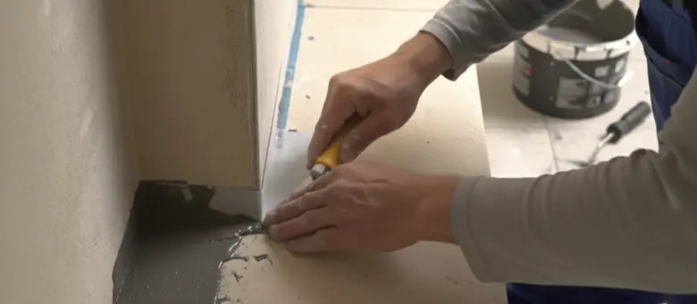 Ruční aplikace šedé hydroizolační hmoty do koutu dlažby