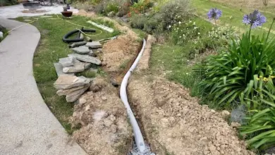 Instalace drenáže pozemku s rourou v příkopu vedle cesty.