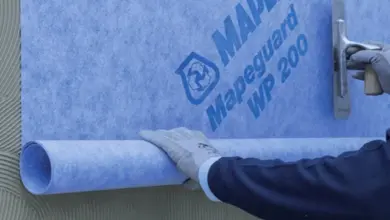 Pracovník aplikuje modrou hydroizolační fólii na zdivo.