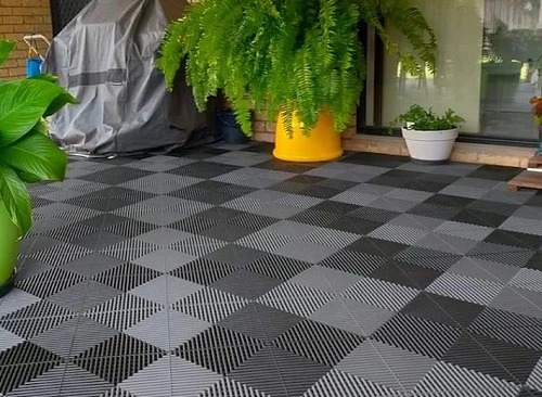 Světle šedé klikací dlaždice na balkóně s rostlinami.
