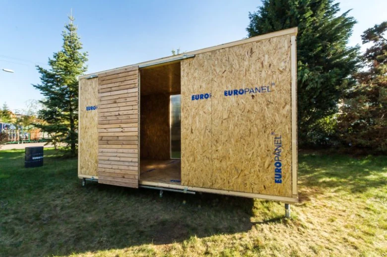 Dřevěný dům z SIP panelů s otevřeným vchodem na trávníku.