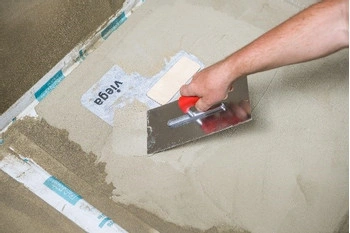 Ruka rozšiřuje lepidlo na podlahu v koupelně pomocí špachtle.