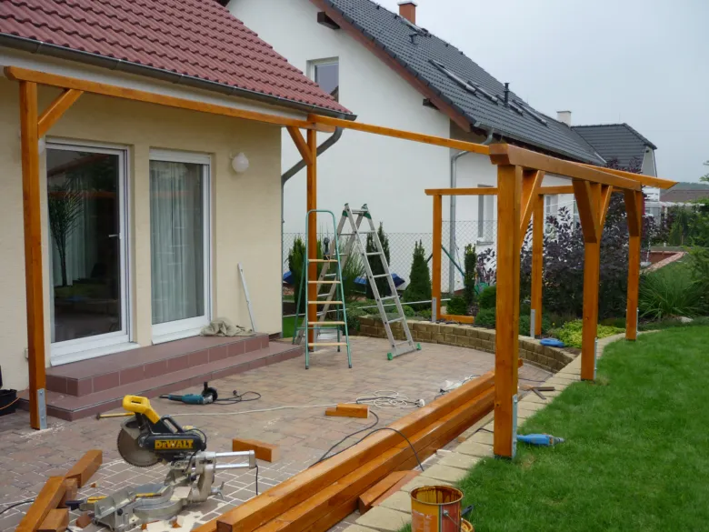 Stavba dřevěné pergoly u cihlové zdi s nářadím a trámy.