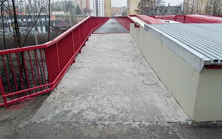 Konkrétní chodník s červeným zábradlím vedoucím do města.