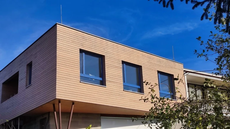 Moderní dům s velkými okny na světlé fasádě pod modrou oblohou.