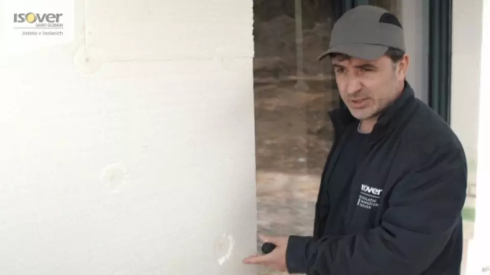 Muž připevňuje polystyrénovou desku ke zdi pomocí lepidlových bodů.