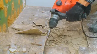 Muž s kladivem odstraňuje staré dlaždice a připravuje podlahu.
