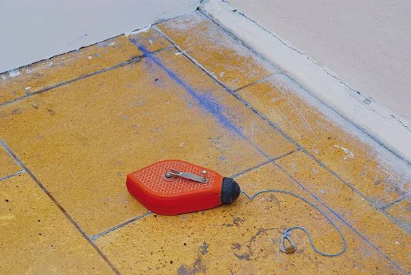 Oranžový laserová úroveň na dlažbě pro výšku stěn.