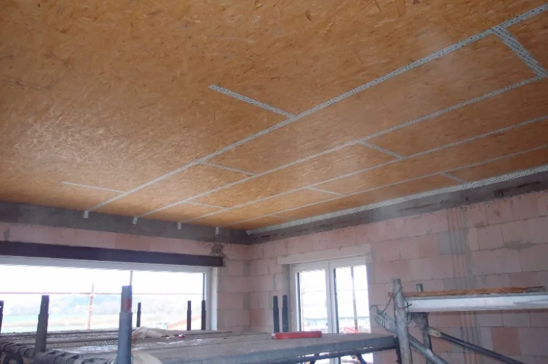 Instalace desek OSB na strop pomocí kovových držáků v průběhu stavby.