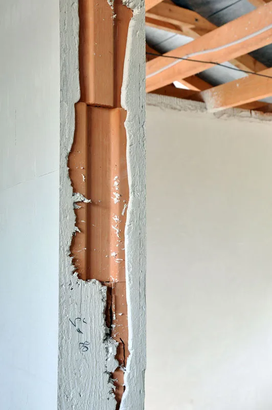 Detail rohu sádrové omítky odhalující dřevěný profil za škrábající se vrstvou.