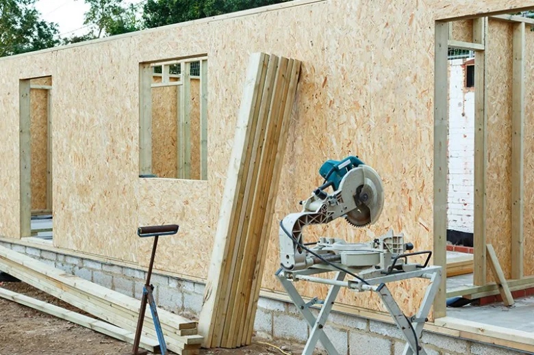 Stavba stěn z OSB desek s nástroji a dřevěnými materiály na místě.