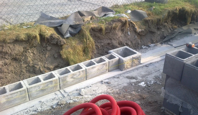 Řada betonových bloků pro základ plotu vedle vykopaného příkopy.