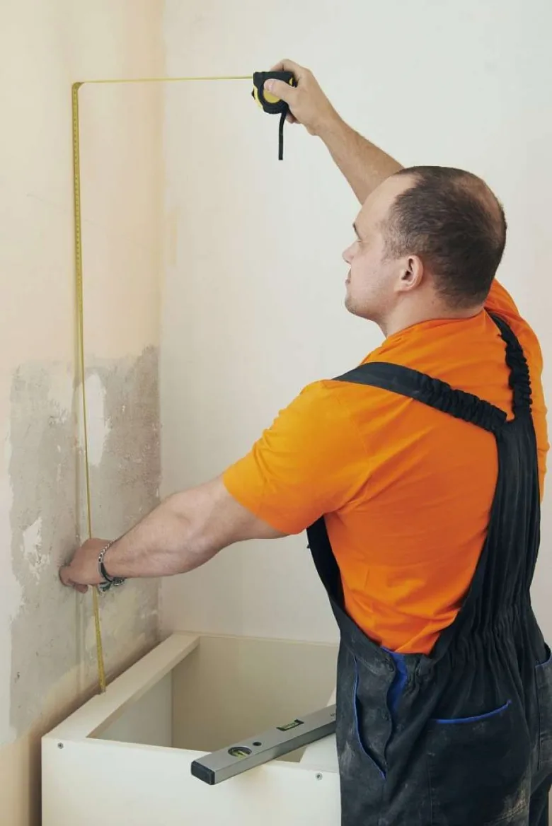 Muž měří zeď pro instalaci kuchyňské skříně s pásmem.