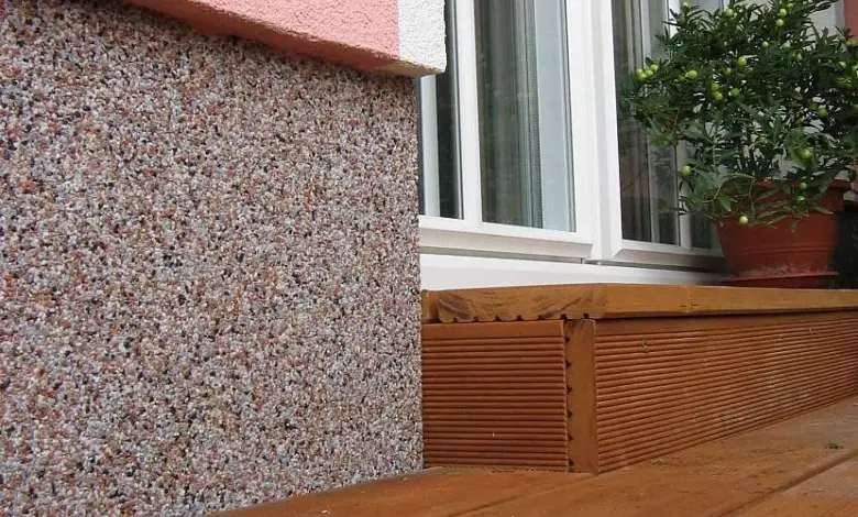 Detail spodní části domu s kamennou omítkou a dřevěným prahem.
