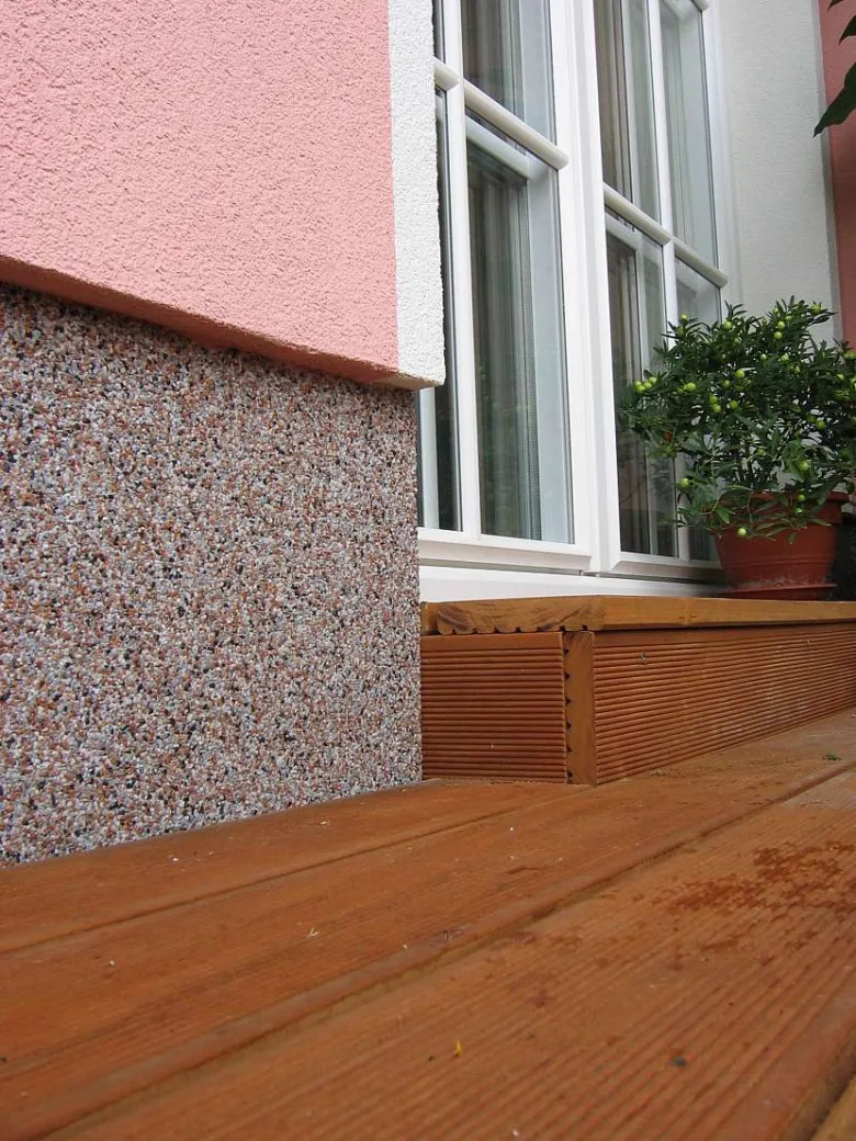 Detail spodní části domu s kamennou omítkou a dřevěným prahem.