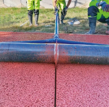 Pracovníci nanášejí červenou hydroizolační vrstvu na betonovou plochu.