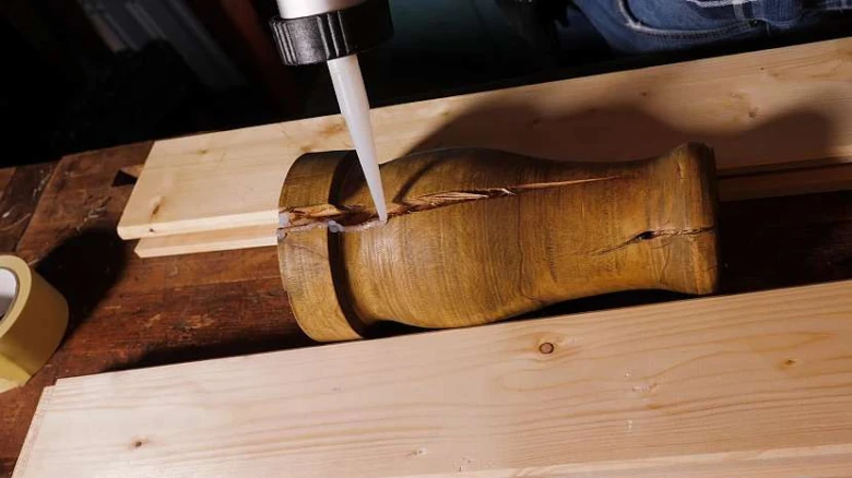 Náplňování praskliny ve dřevě bílým těsnícím materiálem.