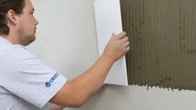 Muž nanáší tmavou omítku na stěnu pod obklady v koupelně.