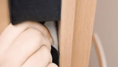 Ruka instaluje černou izolační těsnění do dřevěných dveří.